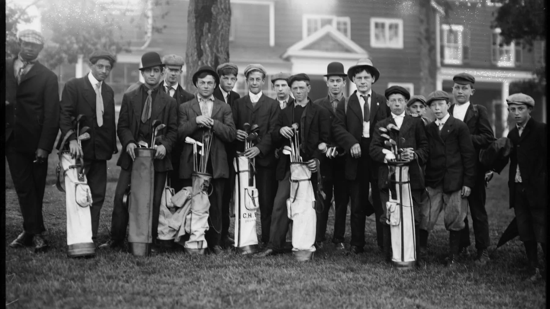 A group of caddies with golf bags outside a clubhouse in the early 1900s