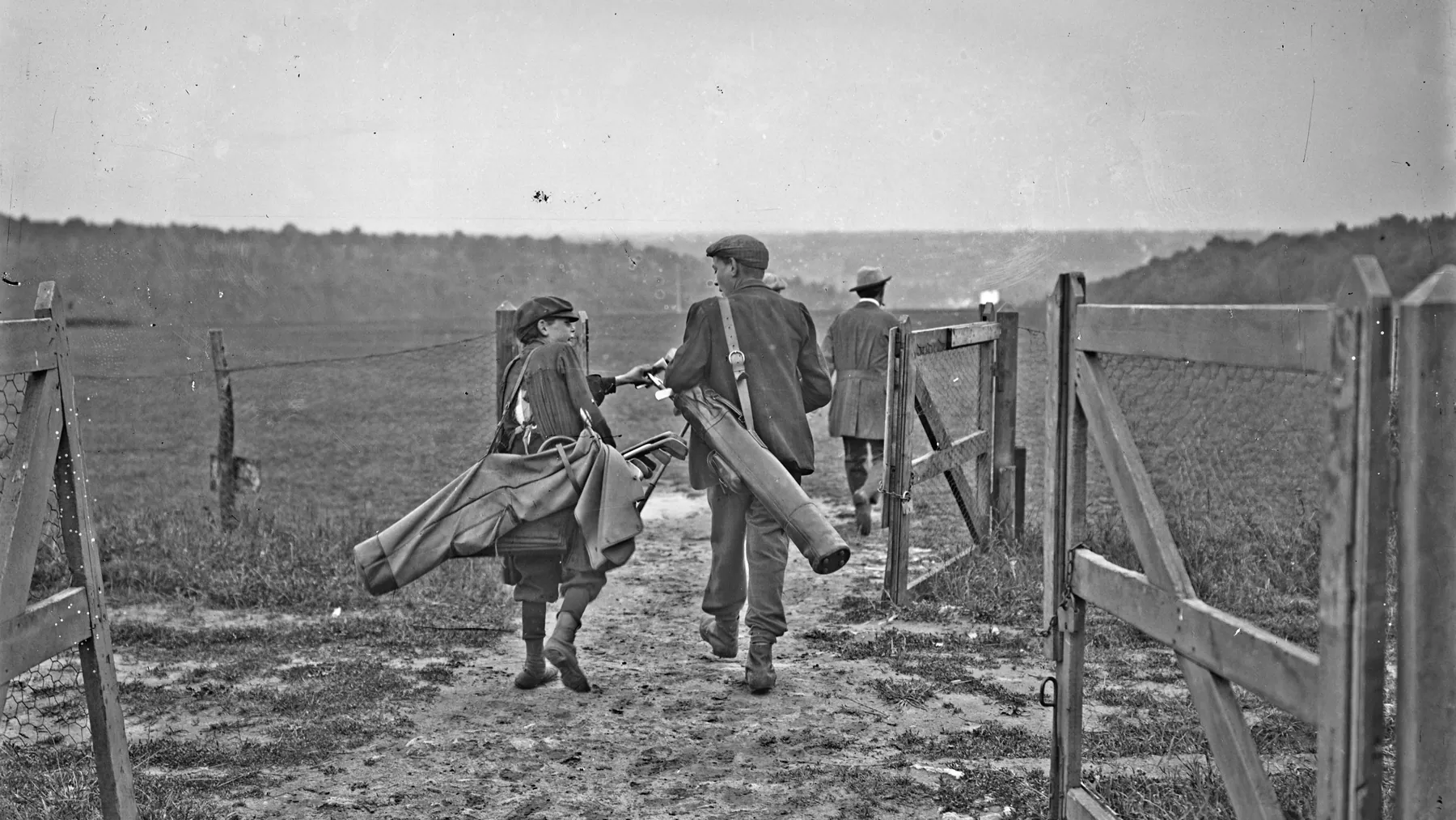 Golfers and caddies walking through a gate onto the course at La Boulie, France, early twentieth century