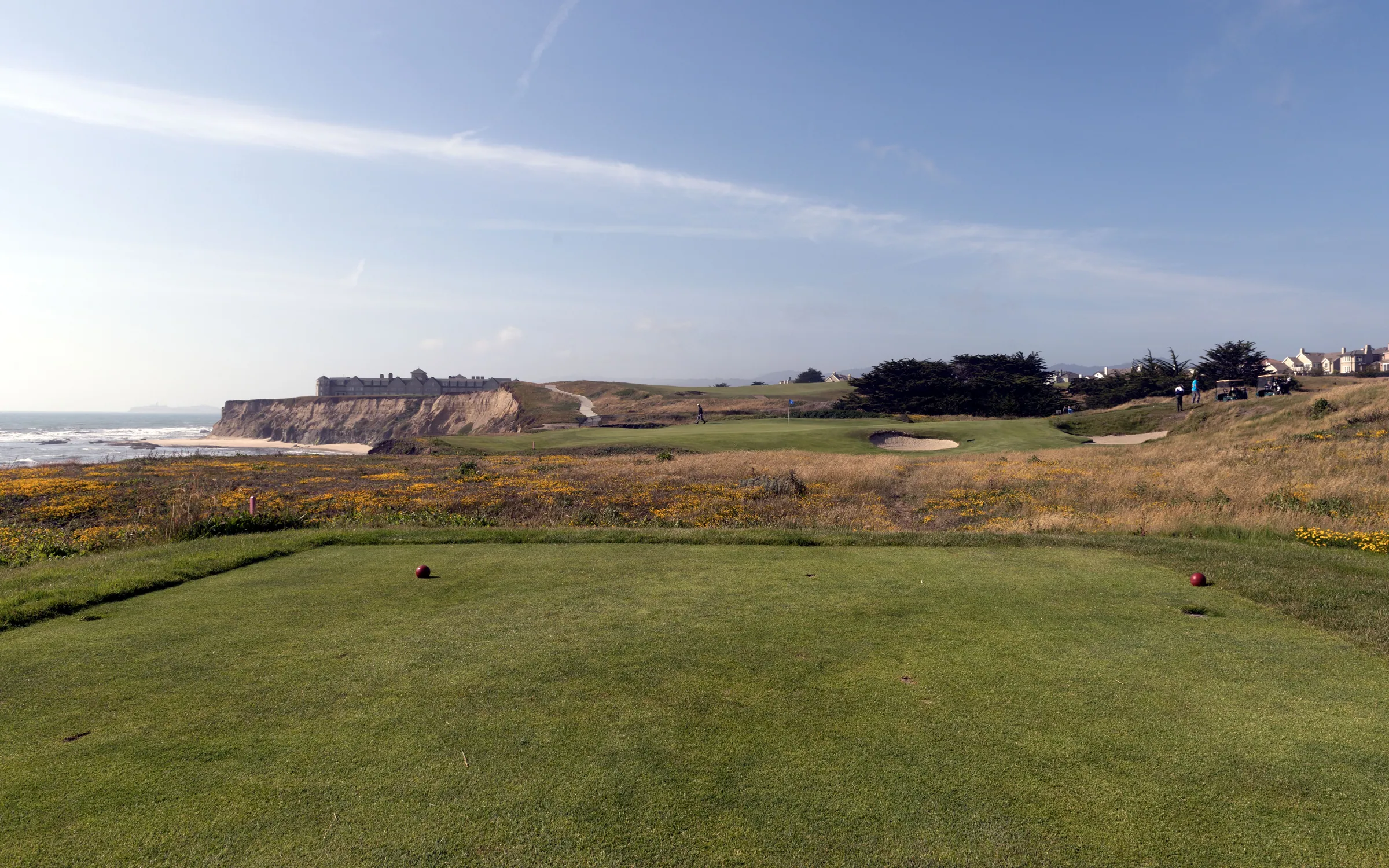A tee box on a clifftop links above the Pacific, the green and ocean beyond