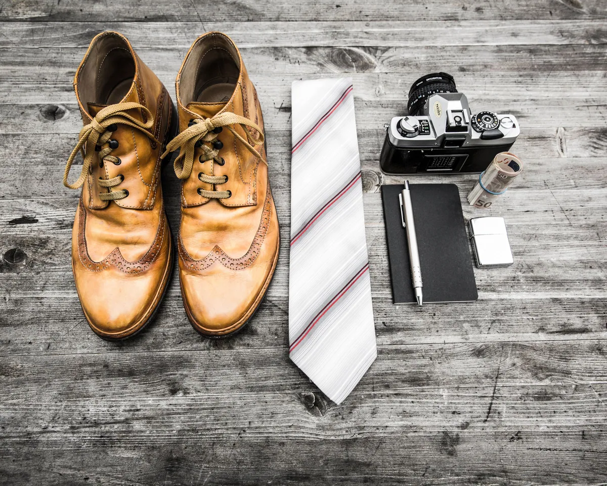Brogues, a striped tie, a notebook and a camera laid out on weathered wood