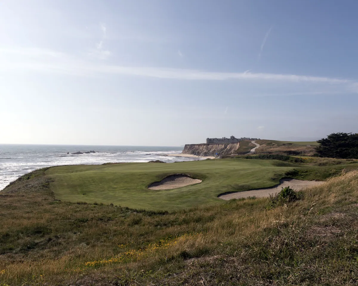 A green guarded by bunkers on a clifftop links beside the ocean