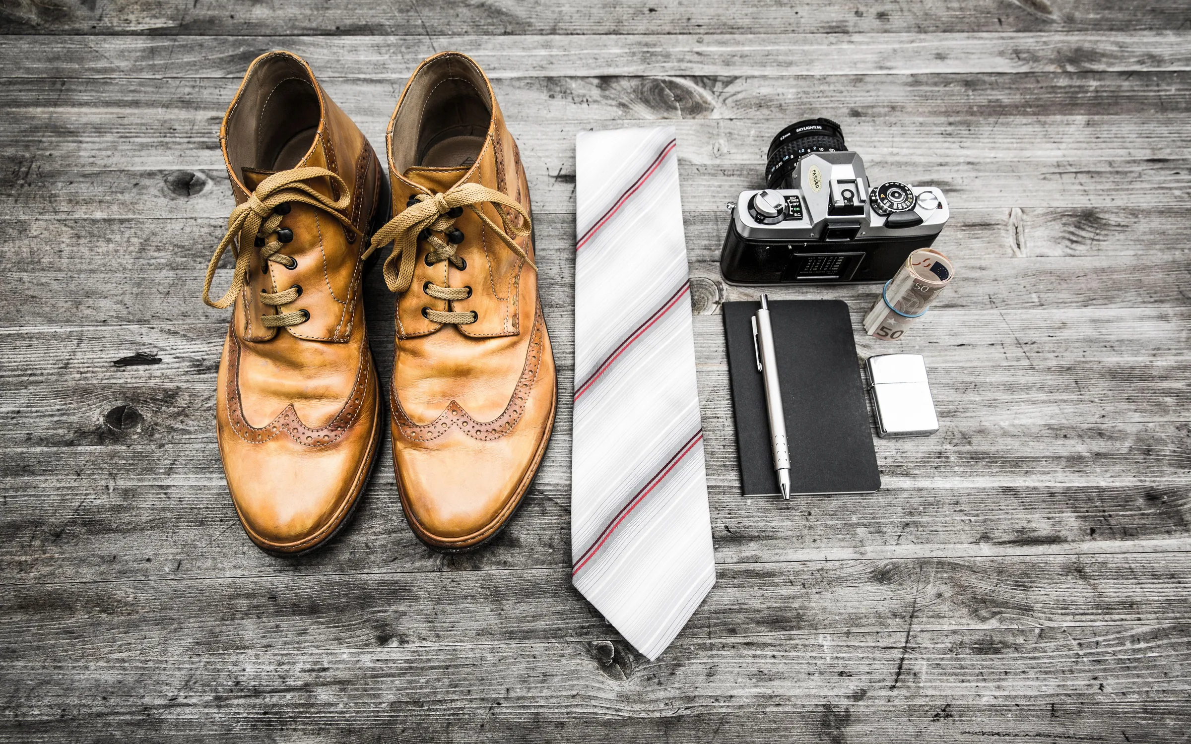 Brogues, a striped tie, a notebook and a camera laid out on weathered wood