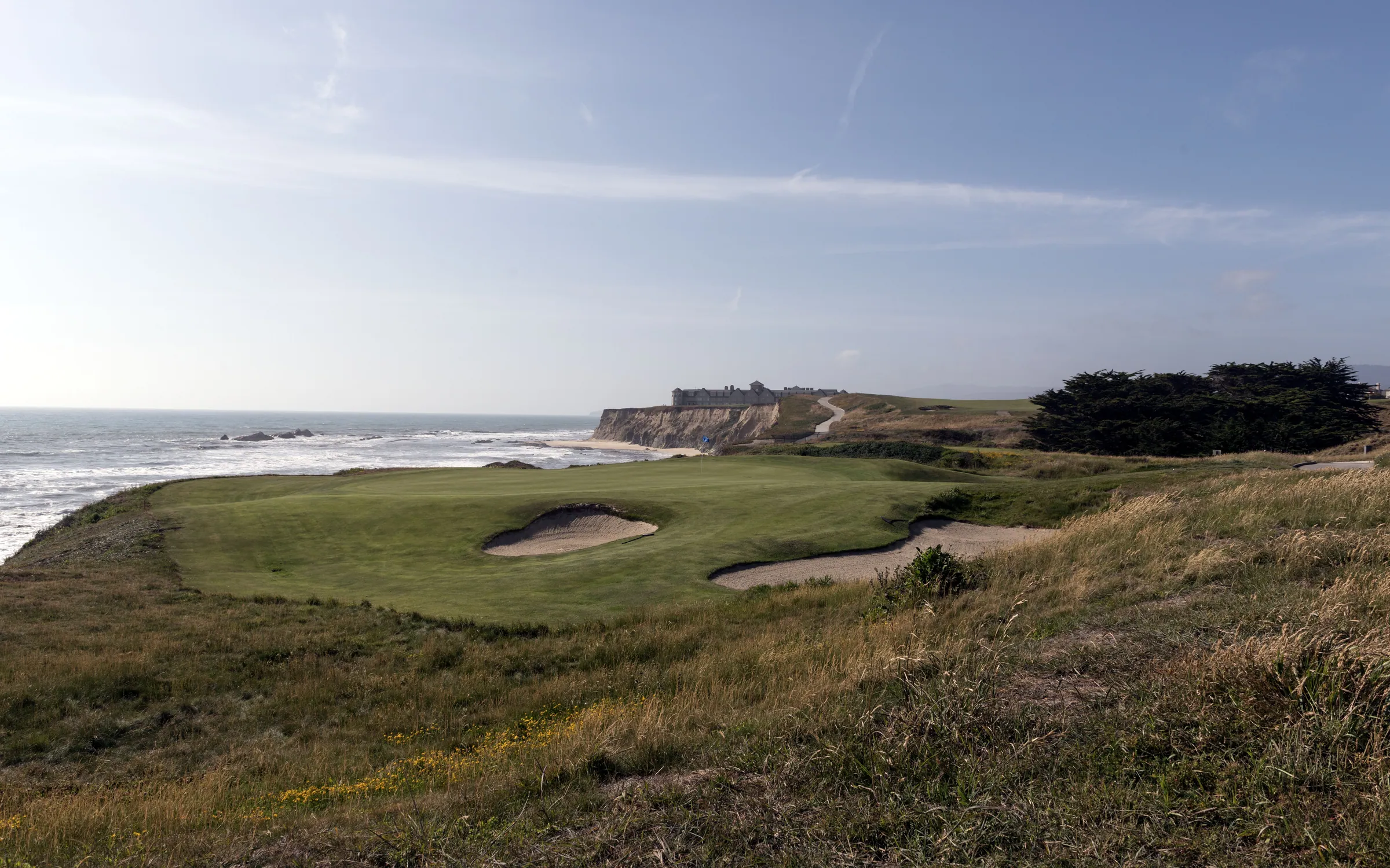 A green guarded by bunkers on a clifftop links beside the ocean